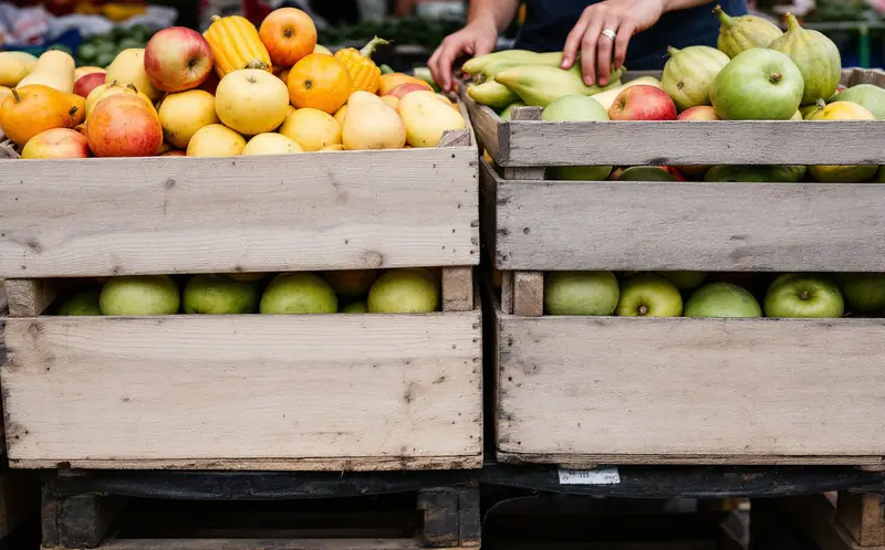 Farmers' market stall with crates of apples, squash and corn under an awning
